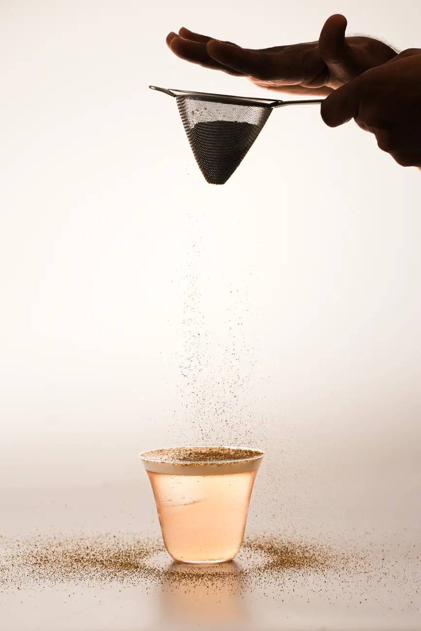Fine powder sifted through a strainer over a small glass